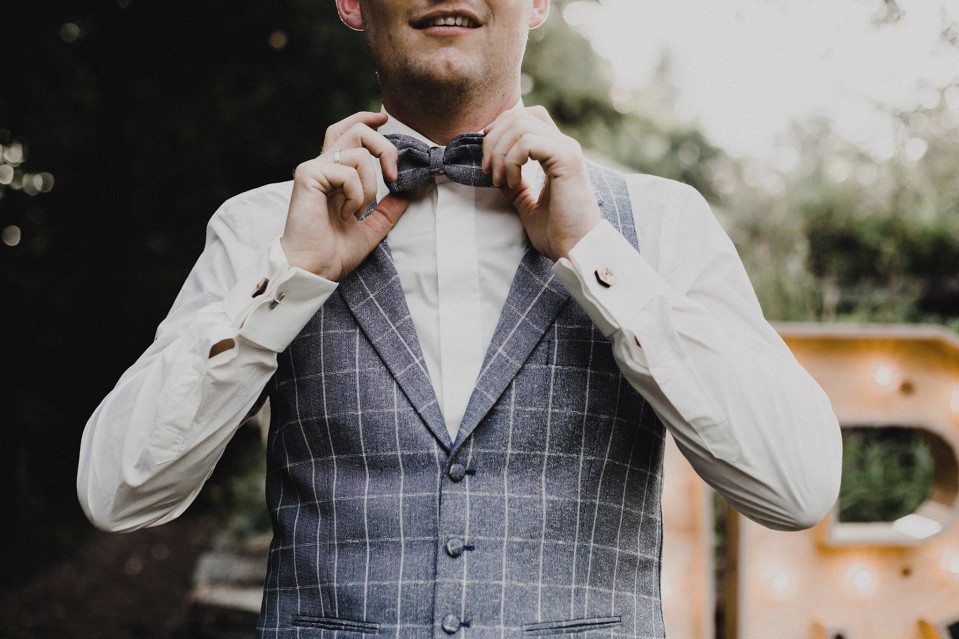 een man in een blauw en wit geruit pak die zijn strikje aanpast