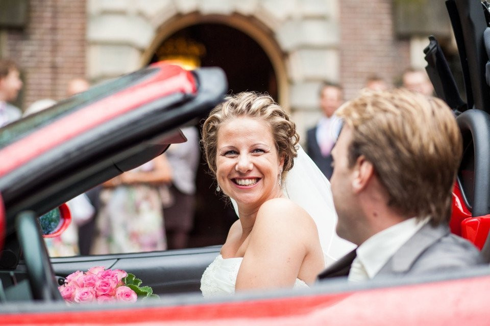 een bruid en bruidegom in een rode cabriolet