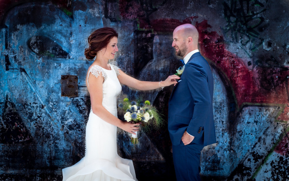 een bruid en bruidegom staan voor een met graffiti bedekte muur