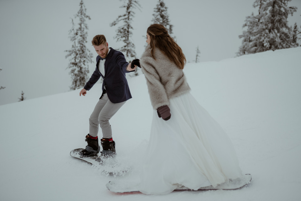een man in een pak en een vrouw in een trouwjurk op een snowboard in het midden van de sneeuw