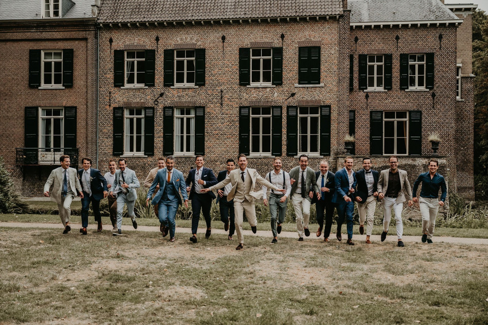 bruidsjonkers in pakken en stropdassen lopen voor een groot bakstenen gebouw