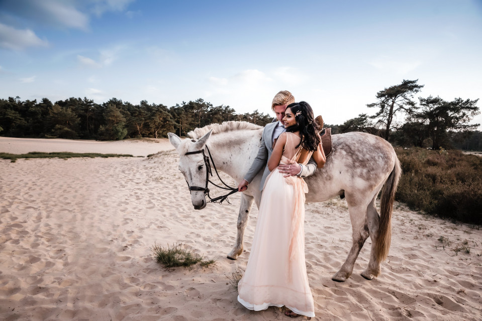 een bruid en bruidegom poseren met hun paard op het strand