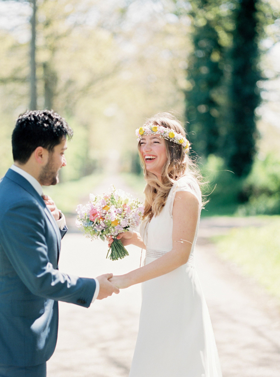 bruid met bloemenkrans lacht volmondig naar haar bruidegom in de buitenlucht