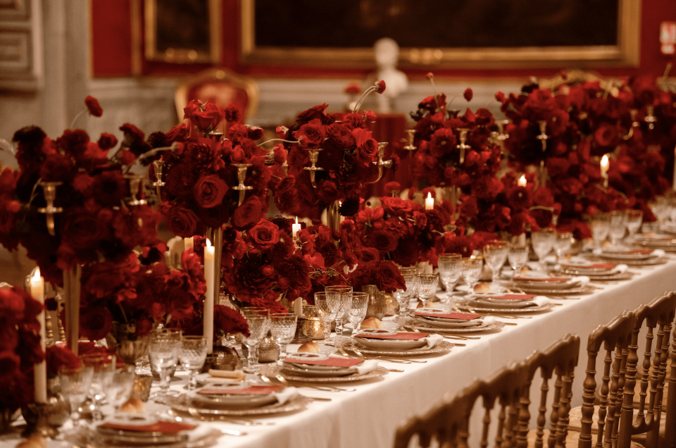 een lange tafel met rode bloemen en kaarsen