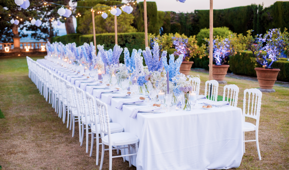 een lange tafel met witte stoelen en blauwe bloemen