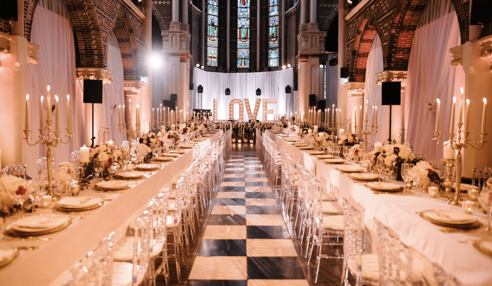 een lange tafel met witte en gouden tafelkleden en kaarsen