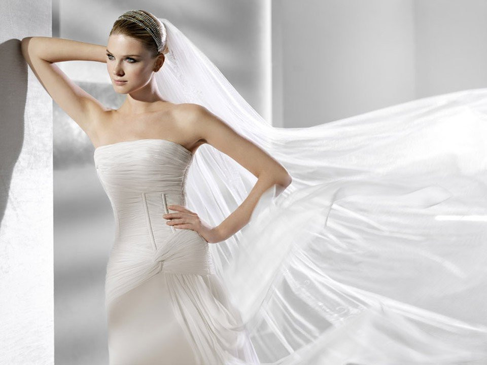 een vrouw in een strapless trouwjurk met haar sluier wapperend in de wind
