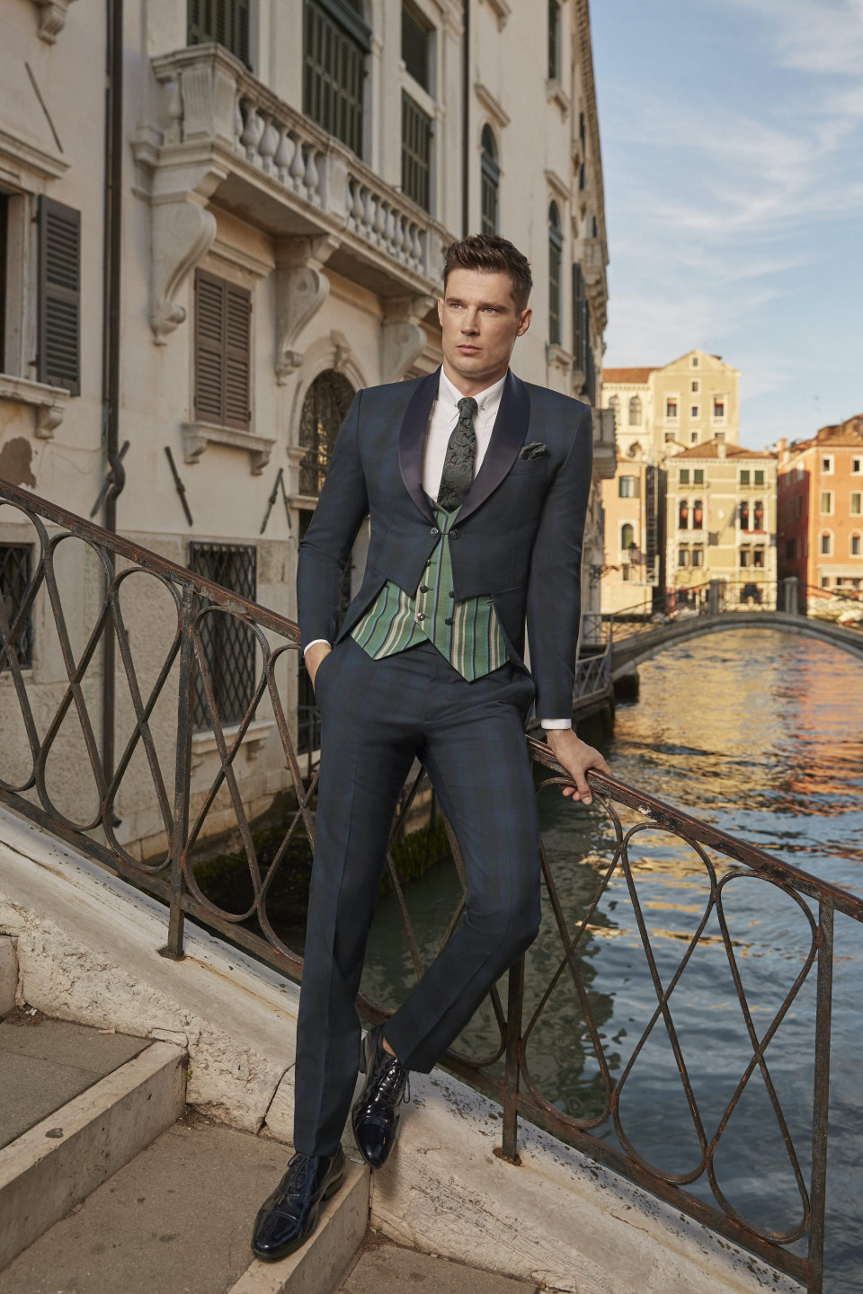 een man in een pak en stropdas leunt tegen een reling