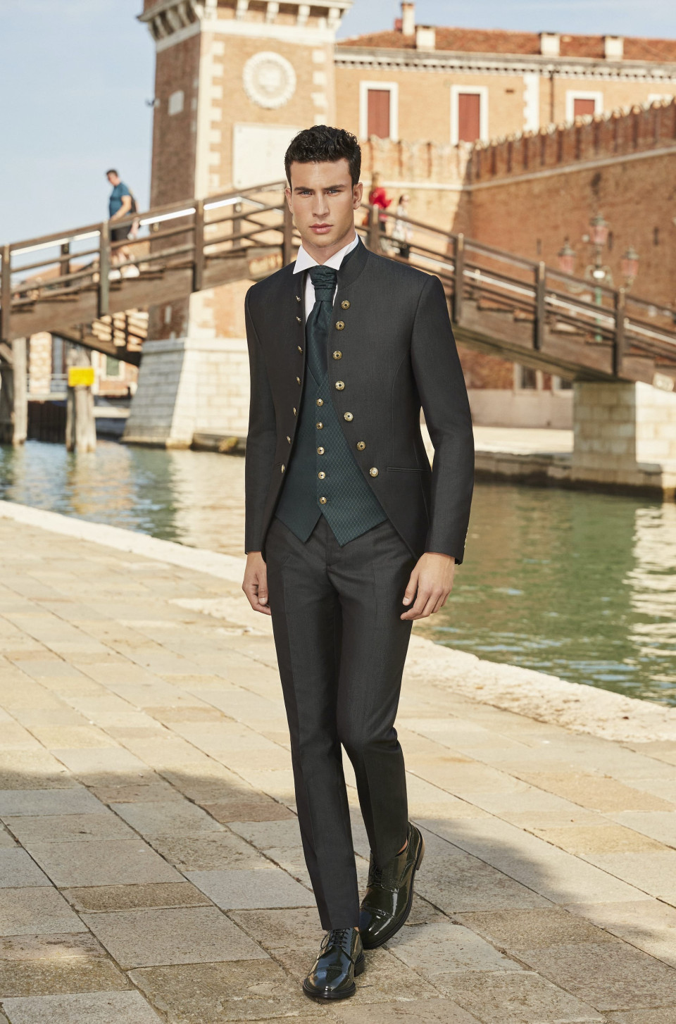 een man in een pak en stropdas loopt langs een gracht