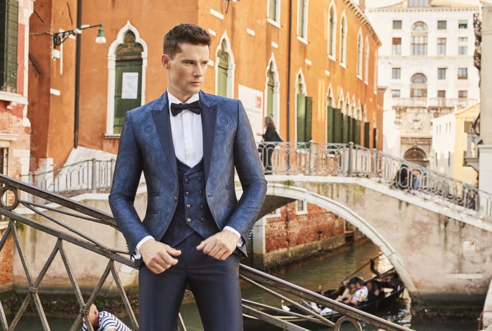 een man in een blauw pak en strik staat op een brug