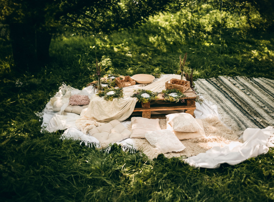 een picknicktafel opgezet in het gras met dekens en kussens