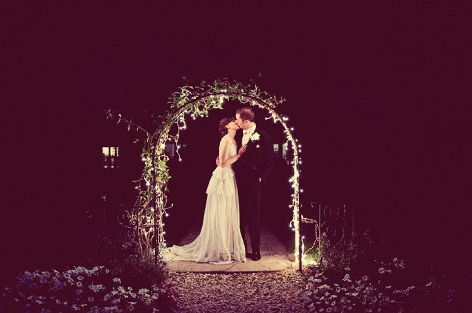 een bruid en bruidegom kussen onder een boog 's nachts