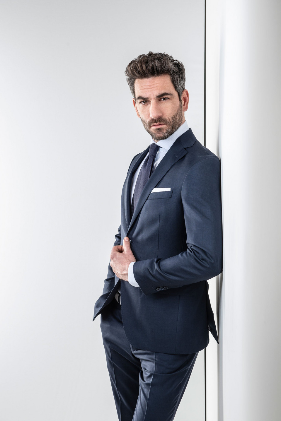 een man in een pak die tegen een muur leunt