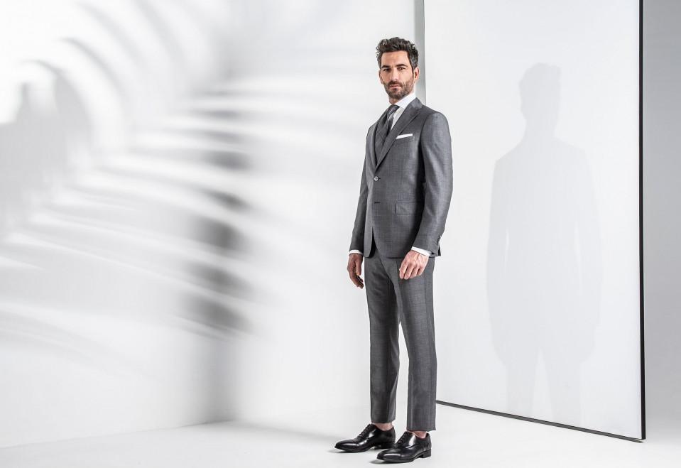 een man in een grijs pak die voor een witte muur staat