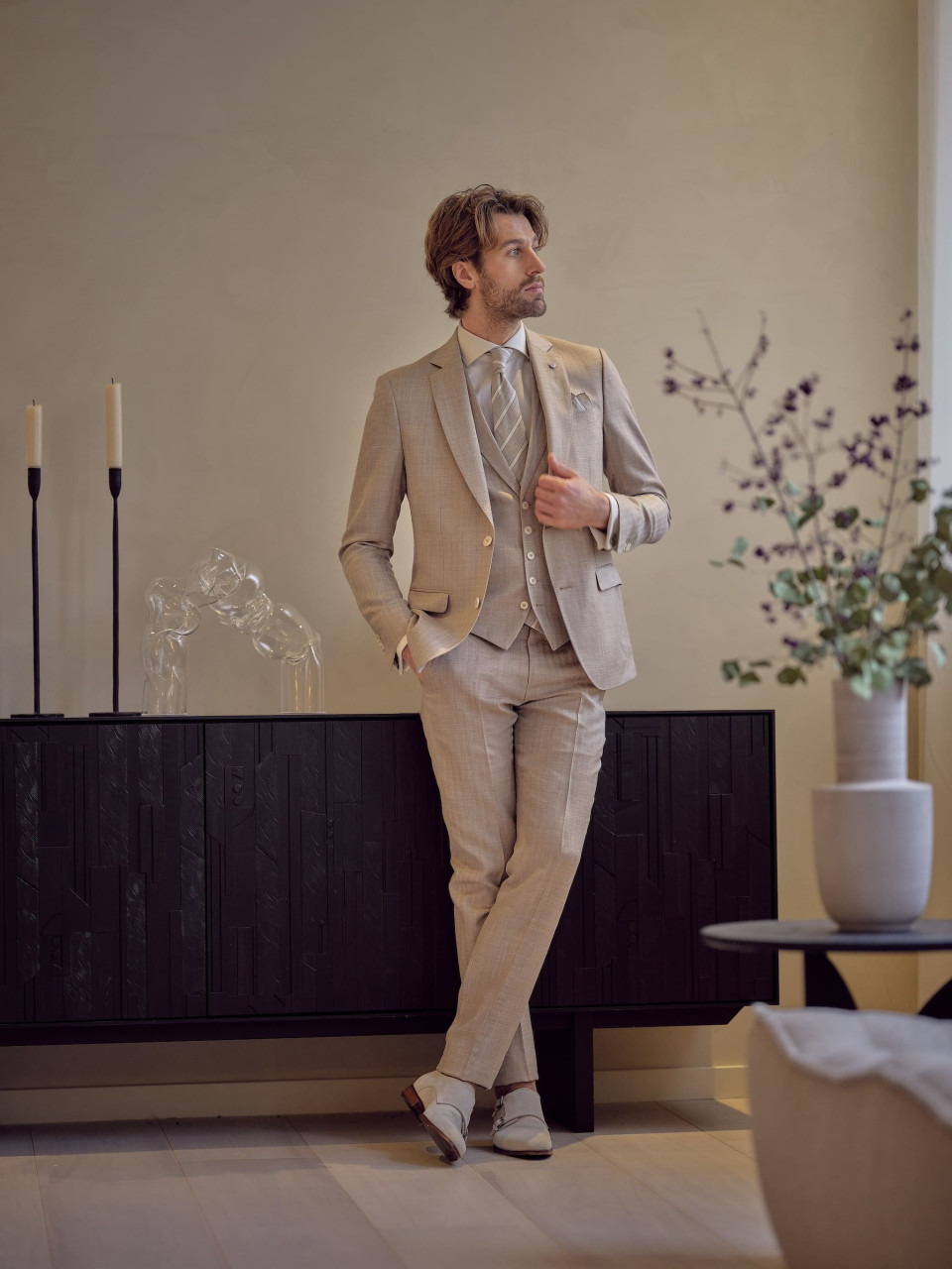 een man in een beige pak en wit overhemd