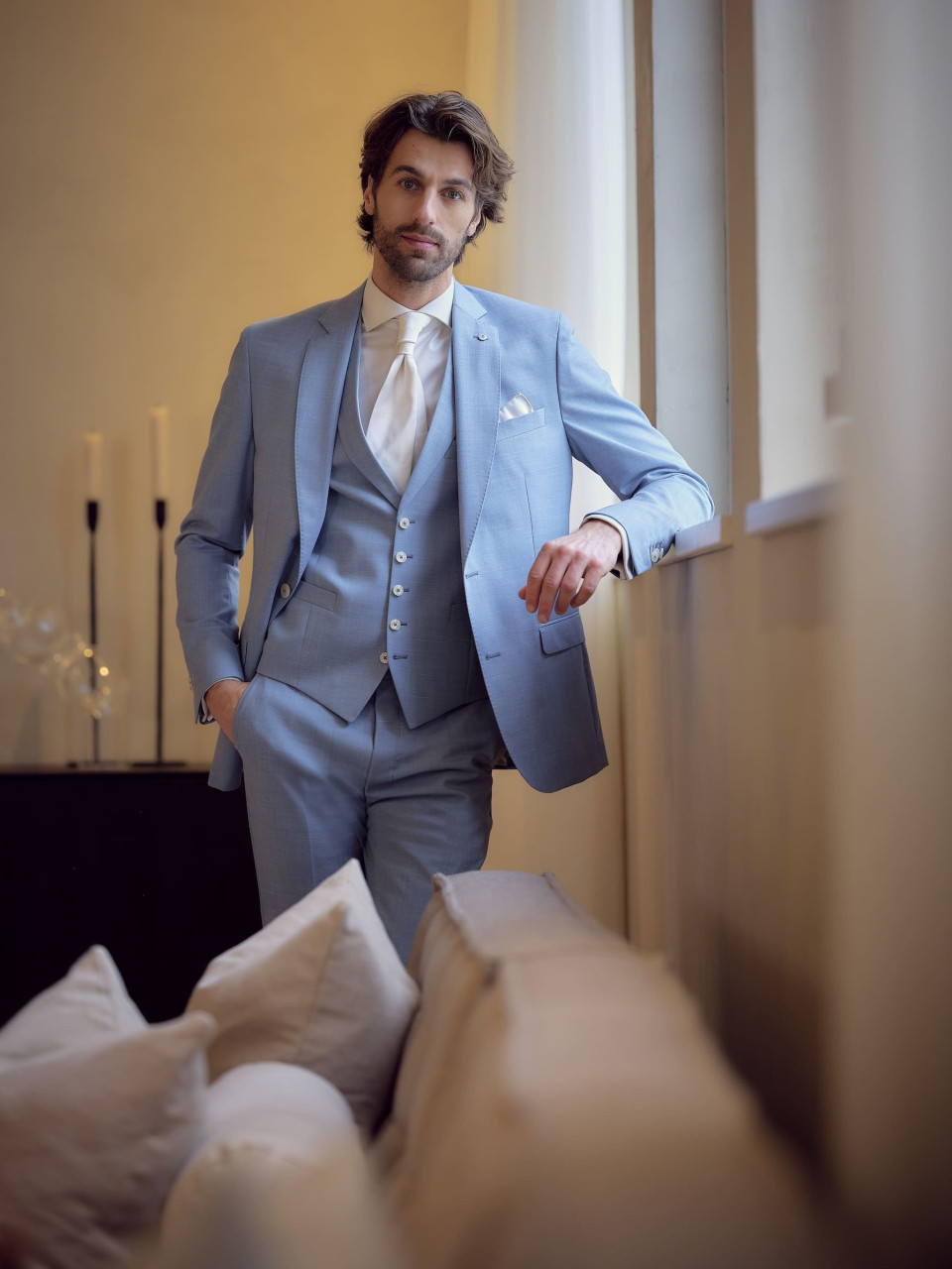 een man in een blauw pak en stropdas die bij een raam staat