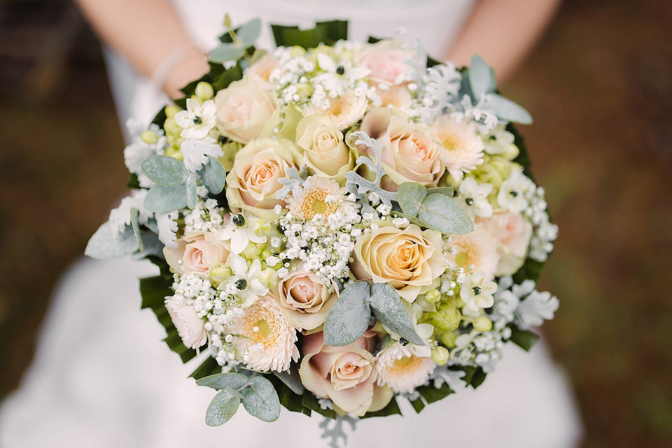 een bruid die een boeket witte en perzikkleurige rozen vasthoudt