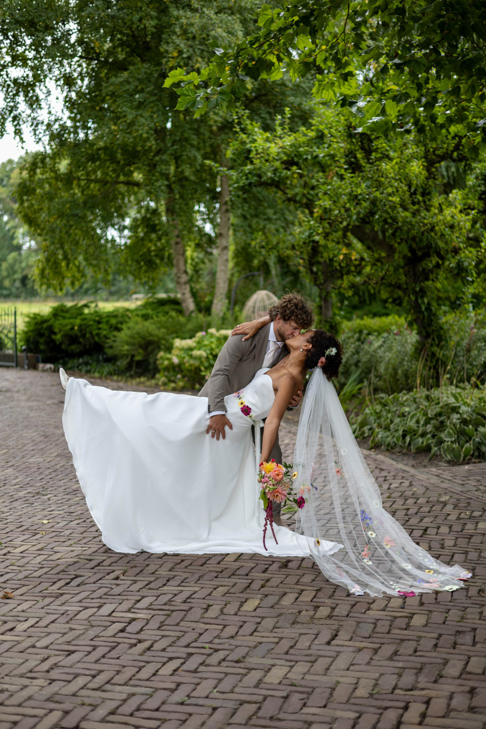 een bruid en bruidegom die kussen op een kinderkopjespad