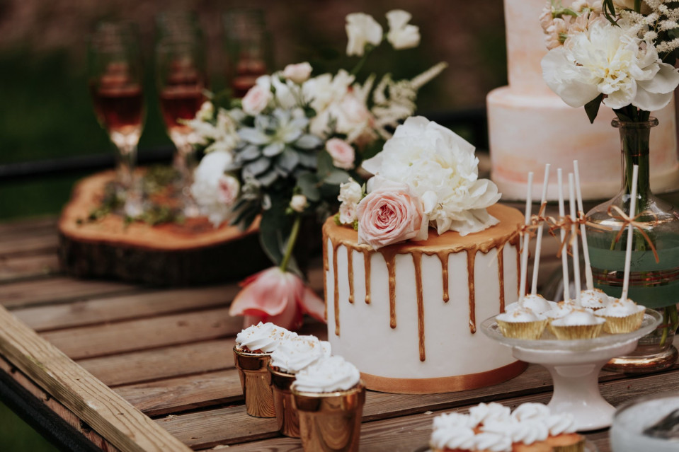 een tafel met een taart, cupcakes en bloemen