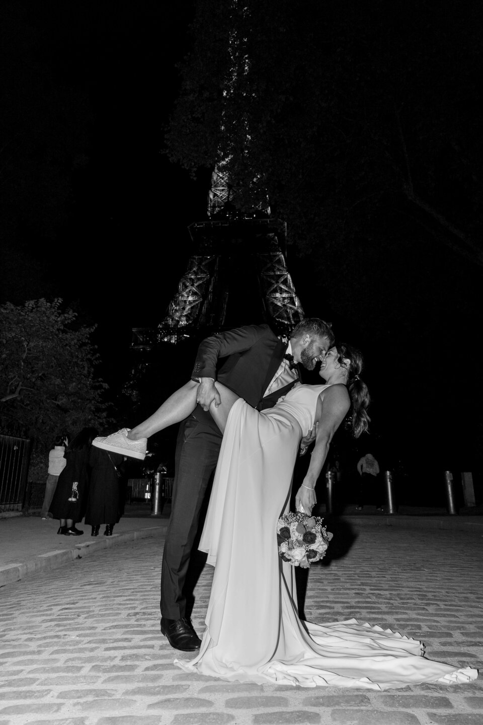 een zwart-wit foto van een bruid en bruidegom die kussen voor de Eiffeltoren