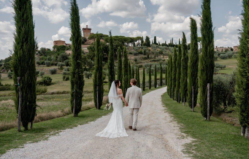 een bruid en bruidegom die over een pad tussen hoge bomen lopen
