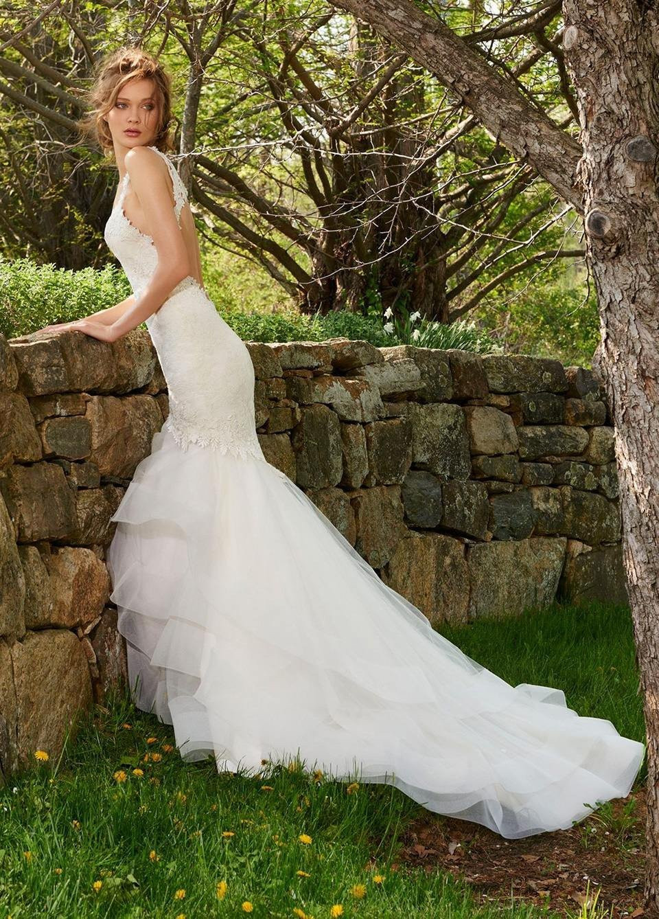 een mooie vrouw in een trouwjurk leunend tegen een stenen muur