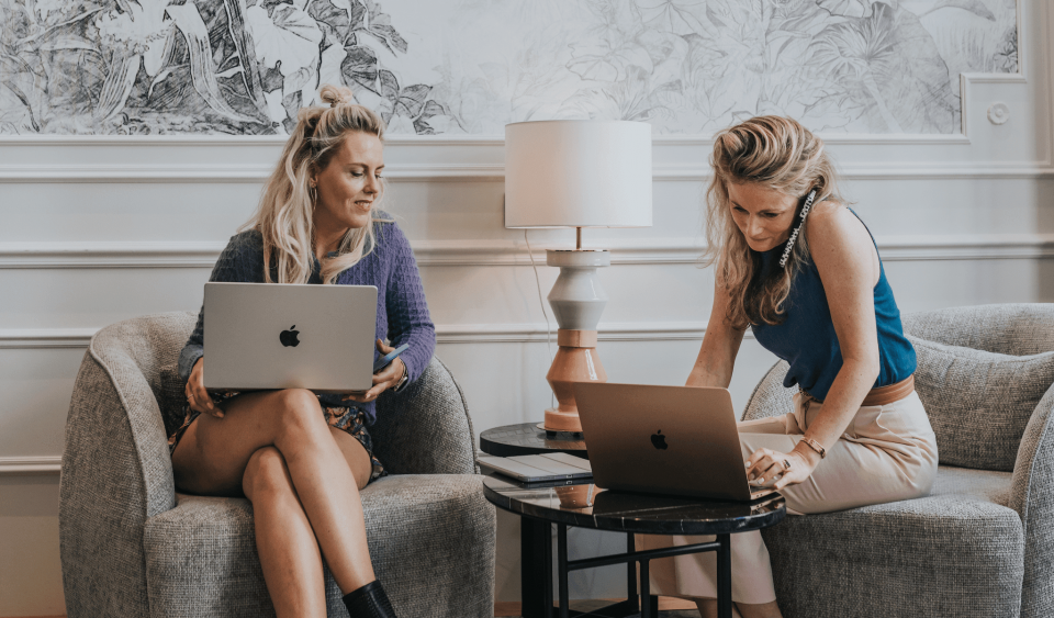 twee vrouwen zitten op stoelen met laptops