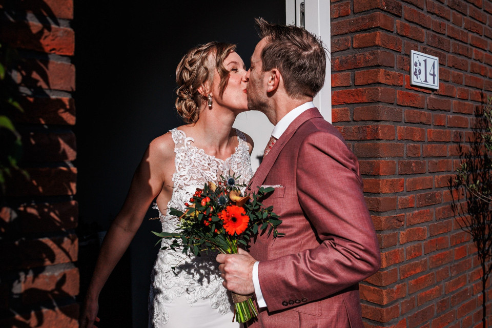 een bruid en bruidegom die voor een bakstenen gebouw kussen