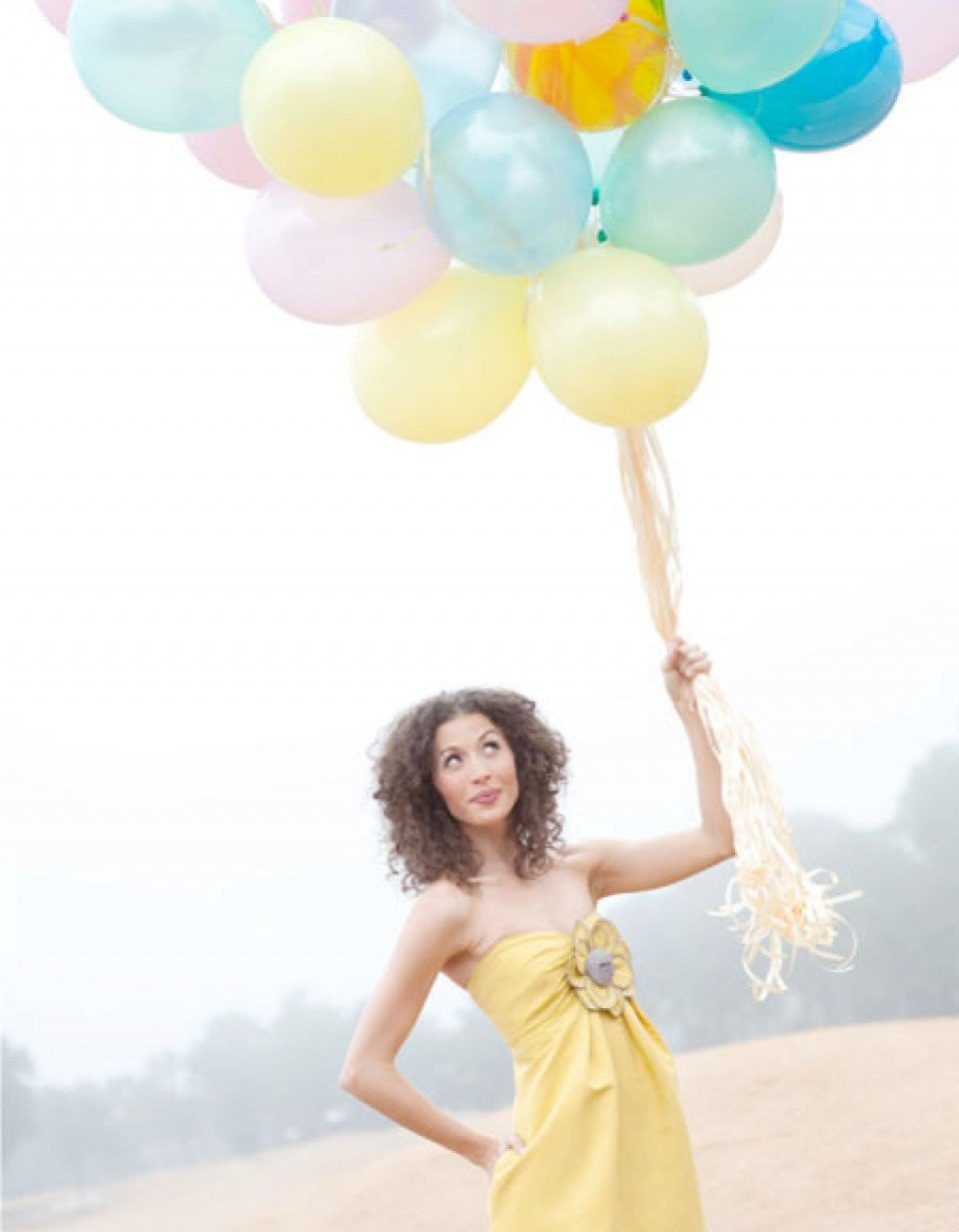 een vrouw in een gele jurk die een bos ballonnen omhoog houdt