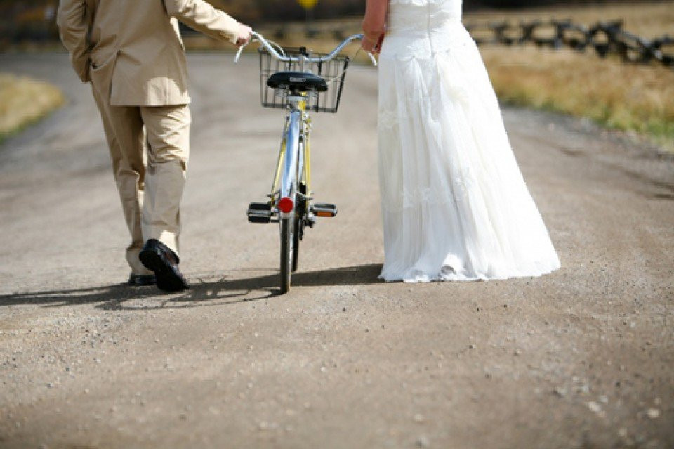 een bruid en bruidegom lopen over een weg met een fiets