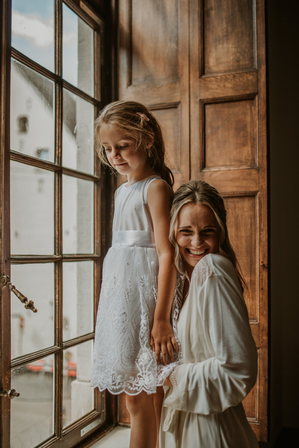 een vrouw en een klein meisje staan voor een raam