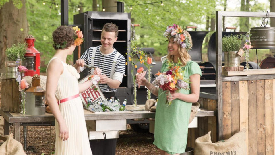 drie vrouwen in jurken staan rond een tafel met eten