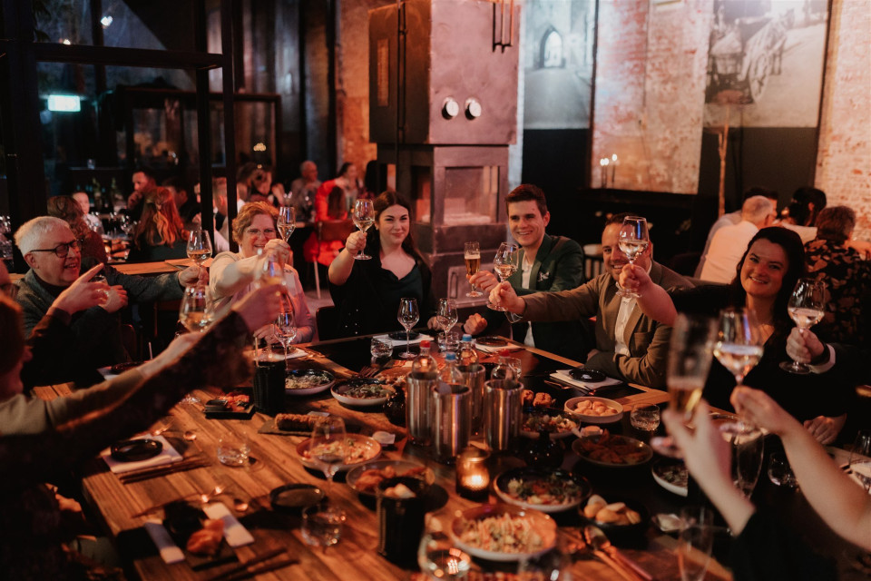 een grote groep mensen die aan een tafel zit met wijnglazen