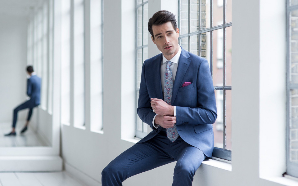 een man in een blauw pak en stropdas zittend op een vensterbank