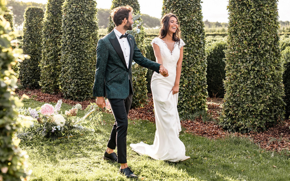 een bruid en bruidegom lopen door een veld van heggen