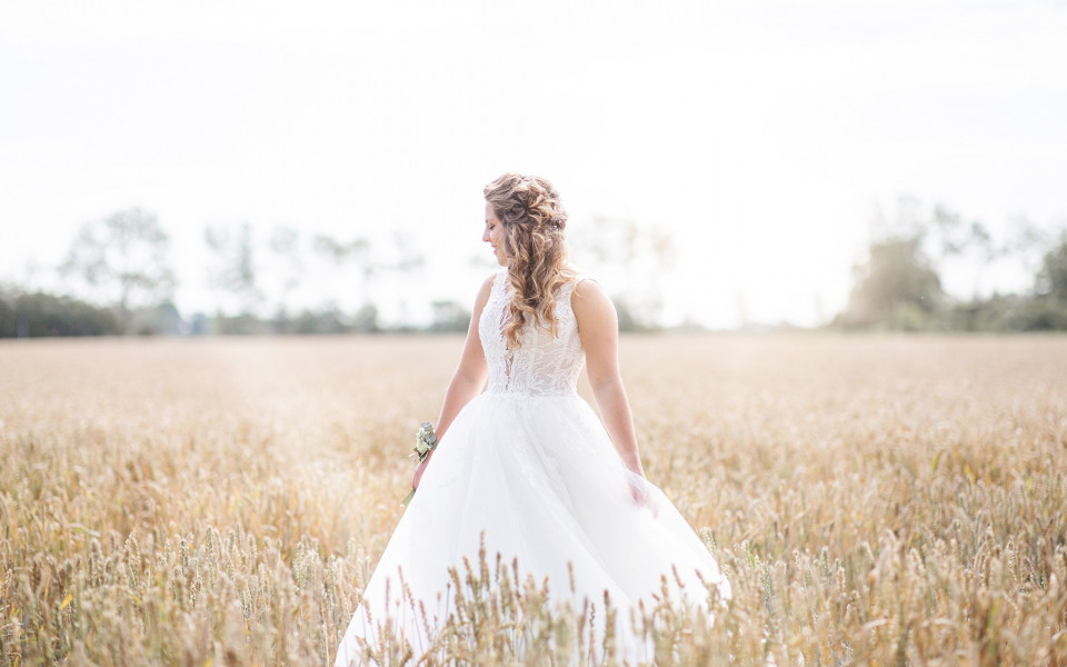 een bruid in een witte jurk die door een tarweveld loopt