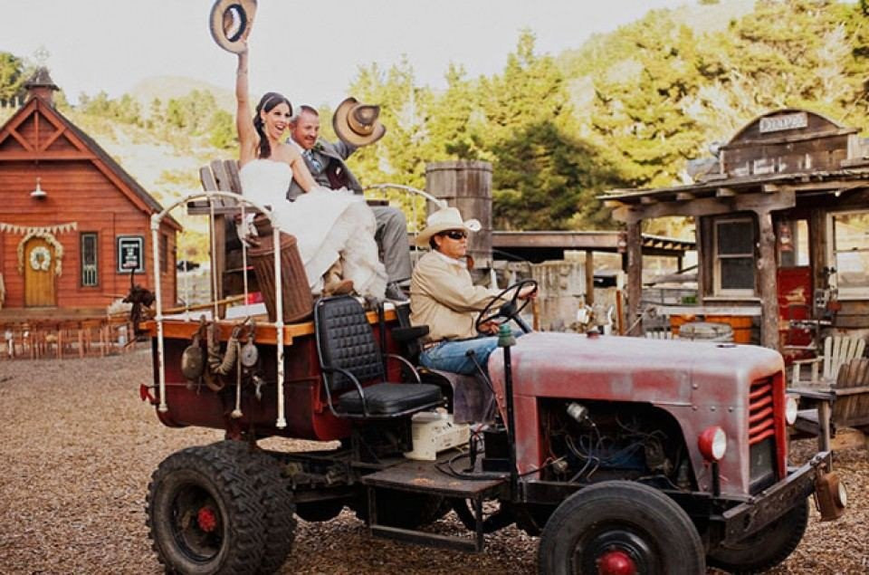 een bruid en bruidegom die op een tractor rijden voor een schuur