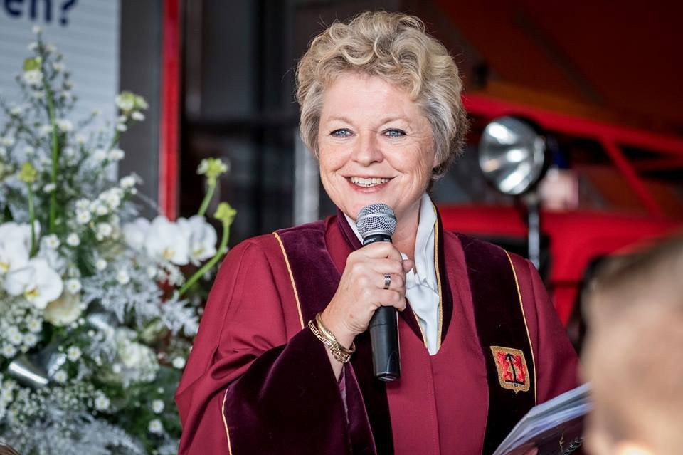 een vrouw in een rode gewaad die in een microfoon spreekt