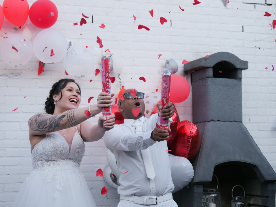 een bruid en bruidegom houden rood en wit confetti vast