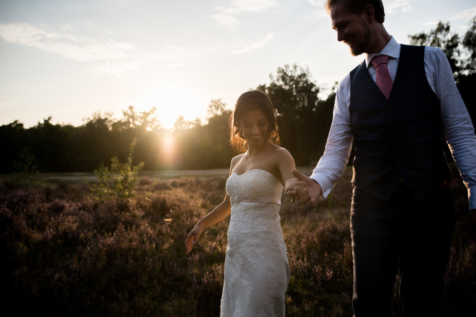 een bruid en bruidegom lopen door een veld bij zonsondergang