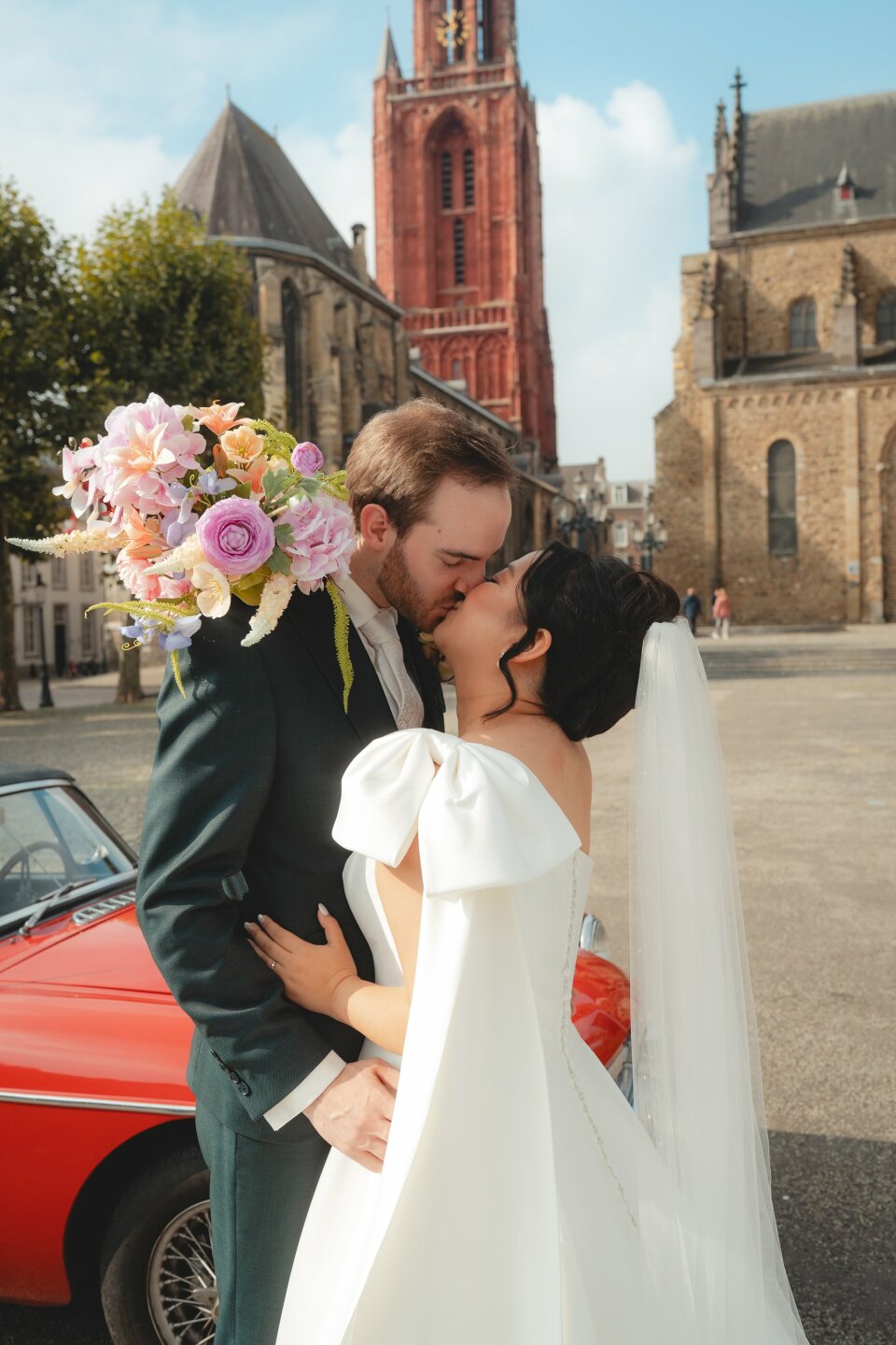 een bruid en bruidegom kussen voor een rode auto