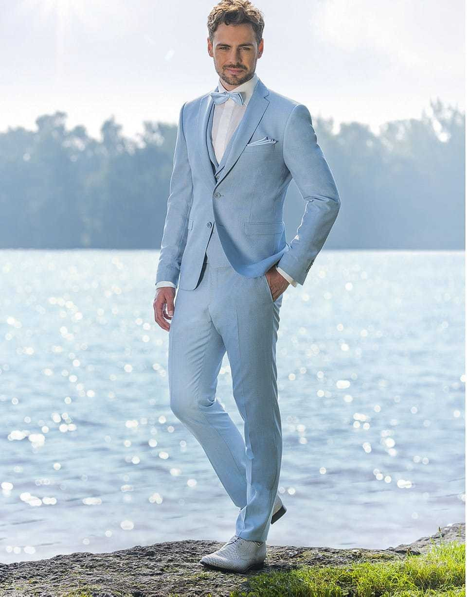 een man in een lichtblauw pak die bij het water staat