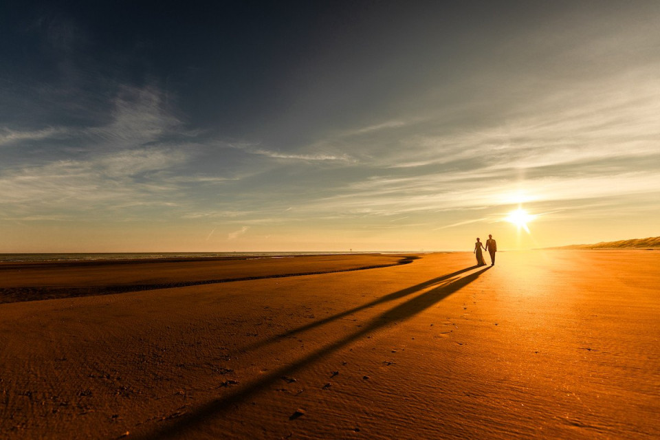 twee mensen die op het strand lopen bij zonsondergang