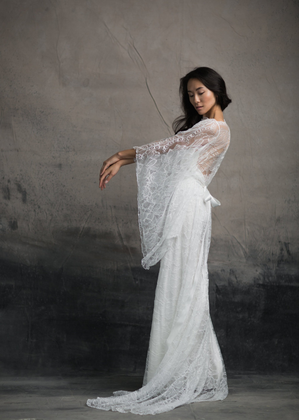 een vrouw in een wit kanten trouwjurk poseert voor de camera