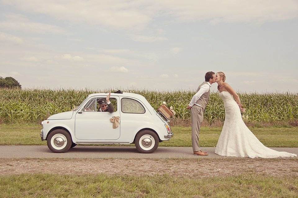 een bruidspaar kust voor een kleine auto