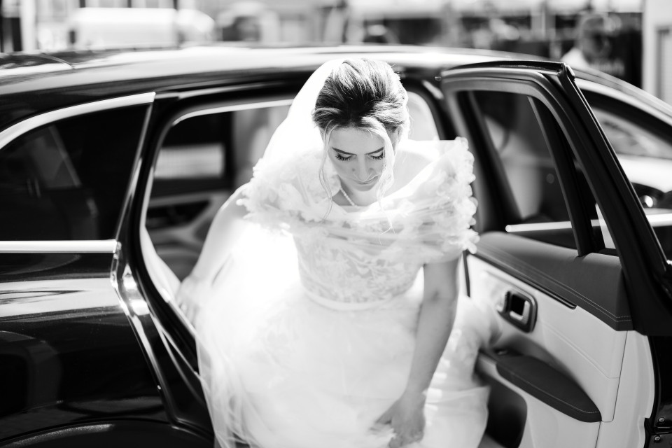 een bruid die uit een auto stapt in zwart-wit
