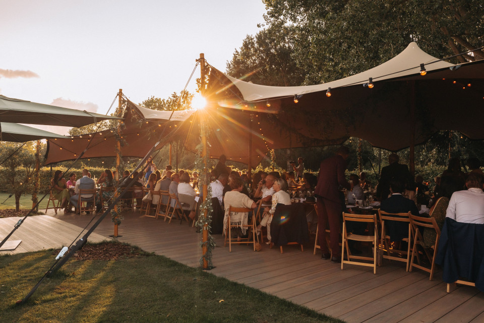 een bruiloft receptie onder een tent met de zon die ondergaat