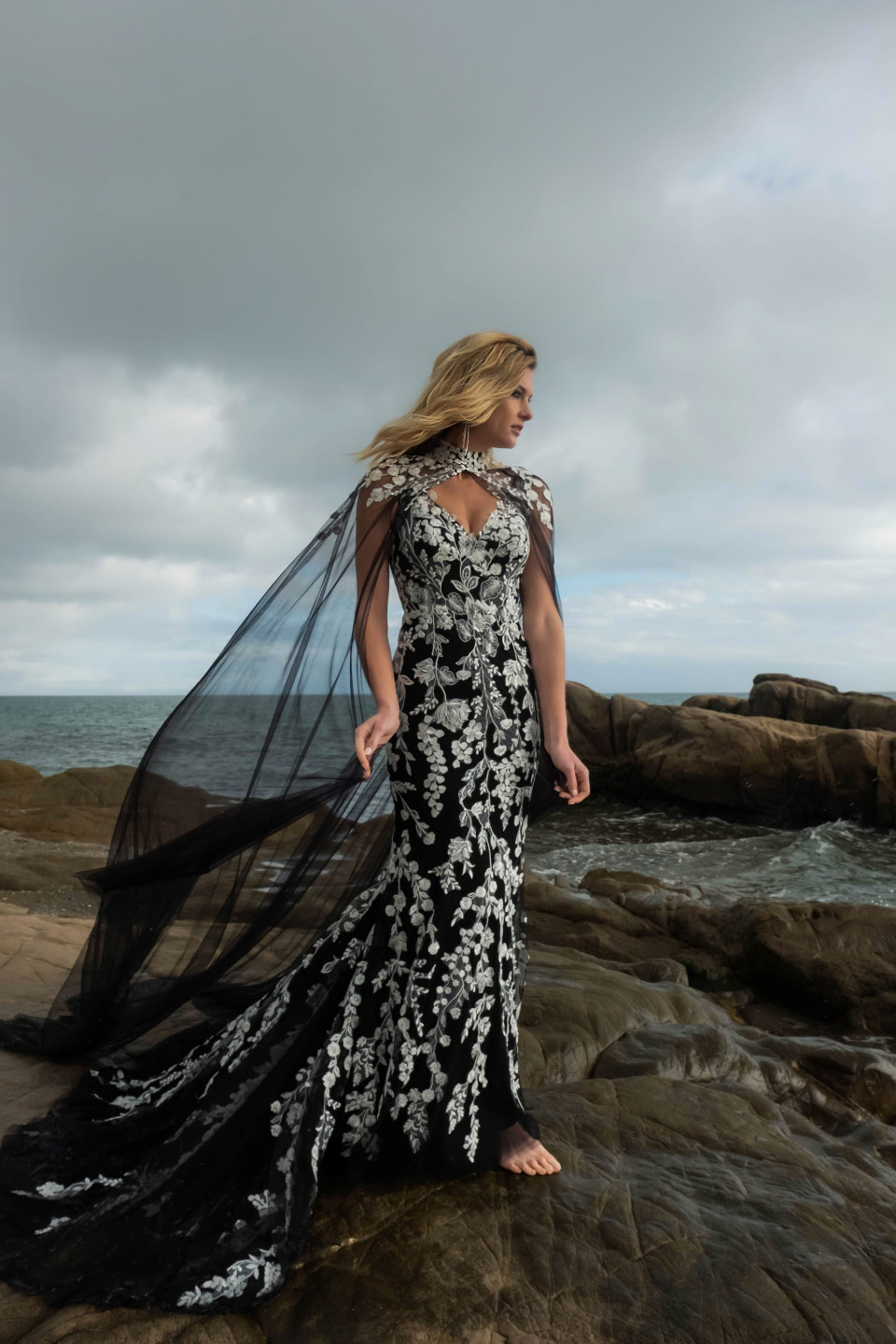 een vrouw in een zwart-witte jurk die op rotsen staat