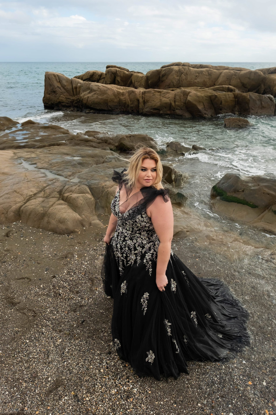een vrouw in een zwarte jurk die op het strand staat