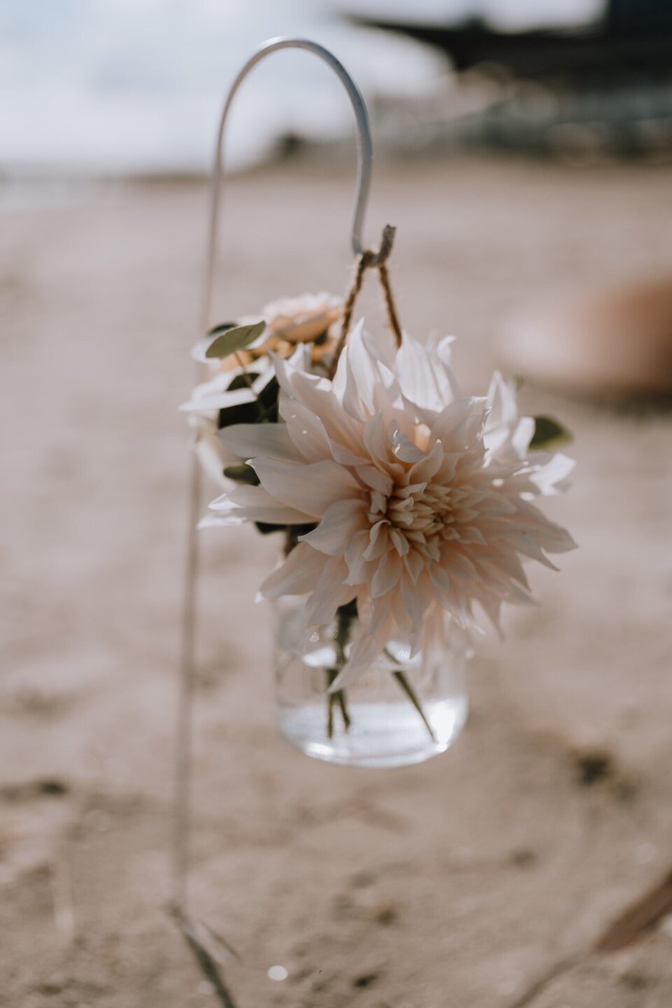 een bos bloemen in een glazen vaas op het strand